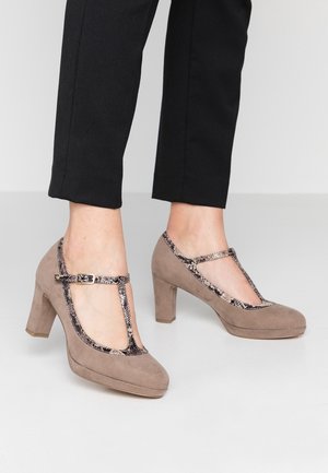 Brązowe zamszowe szpilki mają pasek T w wężowy wzór oraz zaokrąglony czubek, leżąc na gładkiej powierzchni.