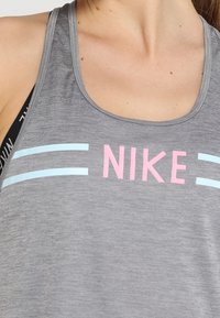 Canotta sportiva grigia con righe orizzontali blu e logo "NIKE" rosa sul petto. Tessuto liscio con scollatura tonda.