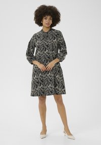 Zwarte jurk met een wit bloemmotief, kraaghals en driekwartmouwen, uitlopend bij de taille. Gekozen met beige hakken.