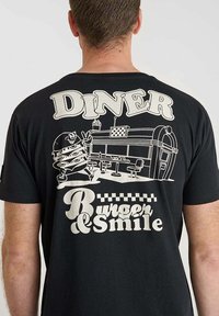 Camiseta de algodón negra con un estampado gráfico de una escena de diner que incluye una hamburguesa de dibujos animados y el texto "DINER Burger & Smile" en blanco.