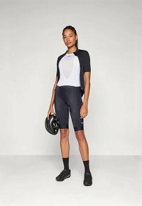 Cyklistický outfit s priliehavou čiernou dresom s krátkym rukávom a bielym spodným dielom, doplnený čiernymi cyklistickými šortkami. Doplnky zahŕňajú prilbu a cyklistické topánky.