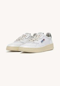 Hvide lædersneakers med beige gummisål, rund tå, perforerede detaljer og snørelukning. Har et sidelogo og grønne accenter.