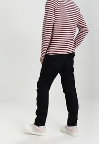 Gestreiftes langärmeliges Hemd in Pink und Schwarz, kombiniert mit schwarzen Hosen und weißen Sneakers mit pinken Akzenten. Legere Kleidung aus der Rückansicht.