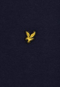 T-shirt bleu marine foncé en coton doux avec un petit logo d'oiseau brodé jaune sur le devant, centré au-dessus de l'ourlet.