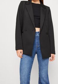 Svart skräddarsydd kavaj med breda slag och två knappar, ihop med formsydda blå jeans som har en mjuk textur och en strukturerad design.