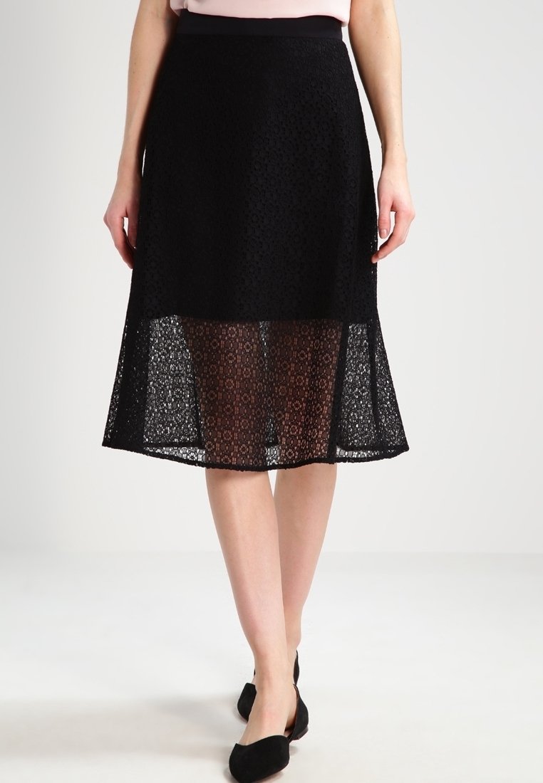 Jupe en dentelle noire avec un motif crochet, dotée d'une ceinture noire unie. L'ourlet est superposé d'un voile transparent pour ajouter de la texture.