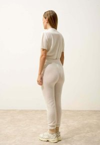 Ljusgräddfärgad stickad outfit bestående av en kortärmad topp och figurnära byxor. Texturen ser mjuk och något fluffig ut, med elastiska manschetter.