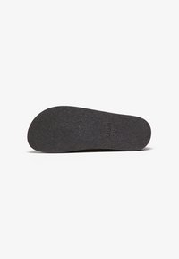 Semelle de chaussure en caoutchouc noir avec une surface texturée, un talon arrondi et un avant plat. Présente un logo en relief sur la semelle.
