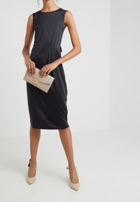 Vestido de satén negro con escote redondeado y cintura fruncida, combinado con un bolso beige con un cierre dorado y tacones altos beige.