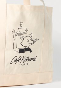 Beige lerret totebag med en svart illustrasjon av en rev som holder en kaffekopp. Teksten "Café Kitsuné Paris" er under designet.