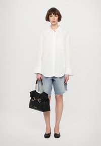 Λευκό πουκάμισο με μακριά μανίκια, ανοιχτό γαλάζιο τζιν σορτσάκι με φθαρμένο στρίφωμα, μαύρη τσάντα χειρός με σχεδιασμό καρδιάς και μαύρες μπαλαρίνες. Απλό, casual στυλ.