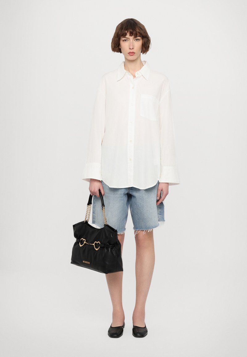 Λευκό πουκάμισο με μακριά μανίκια, ανοιχτό γαλάζιο τζιν σορτσάκι με φθαρμένο στρίφωμα, μαύρη τσάντα χειρός με σχεδιασμό καρδιάς και μαύρες μπαλαρίνες. Απλό, casual στυλ.