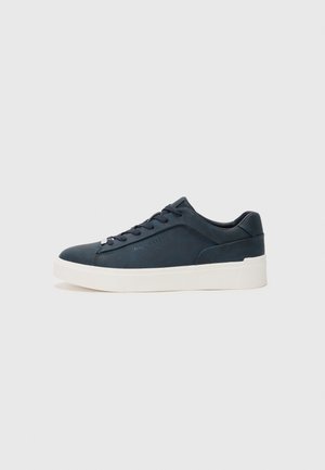 Baskets bleu foncé avec une tige en cuir lisse, bout rond, laçage à l'avant, semelle en caoutchouc blanche et une marque discrète sur le côté.