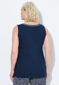 Top senza maniche blu navy con scollatura rotonda e bordi bianchi. Tessuto morbido, texture liscia, indossato con pantaloni a fiori a motivo.