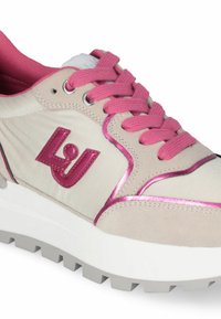 Beige Sneaker mit pinken Akzenten, ausgestattet mit einem strukturierten Obermaterial, pinken Schnürsenkeln und einer stabilen weißen Sohle mit einem grauen Profil.