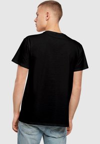 Melnas kokvilnas t-krekls ar īsām piedurknēm un klasisku apaļu kakla izgriezumu; gluda tekstūra, nav redzamu rakstu vai grafikām, attēlā redzama aizmugurējā skata.