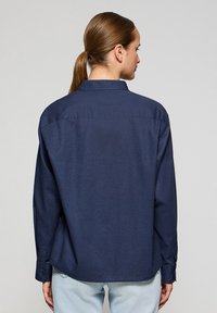 Dunkelblaues Langarmhemd mit Kragen, Knopfmanschetten und lässigem Schnitt. Glattes Gewebe mit subtiler Struktur.