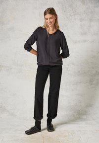 Top leggero nero a maniche lunghe con scollatura a V, abbinato a pantaloni neri larghi e scarpe slip-on con borchie rotonde e risvolti.