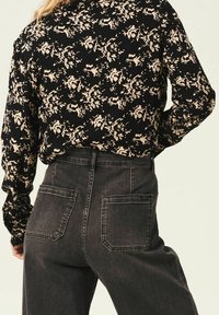 Camicia a maniche lunghe nera con motivo floreale e righe beige, abbinata a jeans in denim grigio scuro a vita alta con due tasche posteriori.