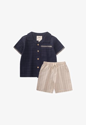 Camisa de cuadros azul marino de manga corta con botones de madera y bolsillo; pantalones cortos beige con rayas verticales y cintura con cordón.