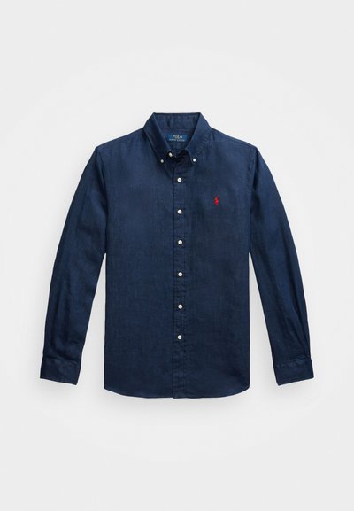 Camisa de manga longa azul marinho em linho, com colarinho abotoado e um pequeno logo vermelho no lado esquerdo do peito. Textura suave, design minimalista.