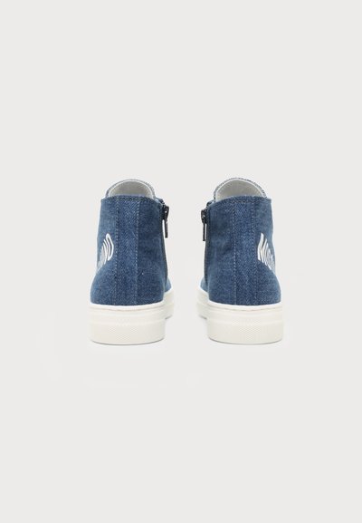 Paire de baskets montantes en denim bleu avec semelles blanches, vues de dos sur un fond uni clair.
