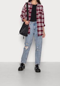 Röd och vit rutig flanellskjorta över en svart topp, ljusblå slitna jeans och svarta plattformsskor. Har en svart väska.