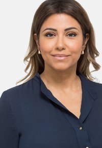 Camicia blu navy con colletto e chiusura a bottoni, realizzata in un tessuto morbido e con una texture liscia. Orecchini in tono oro aggiungono un accento sottile.