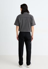 Gray short-sleeve shirt with a collar, paired with black pants featuring side pockets, viewed from the back against a light background.