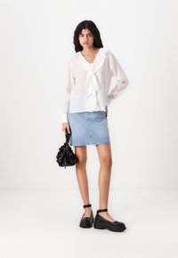 Blusa blanca texturizada con cuello acampanado, combinada con una falda de mezclilla azul claro. Zapatos negros de suela gruesa y un bolso negro con flores completan el look.