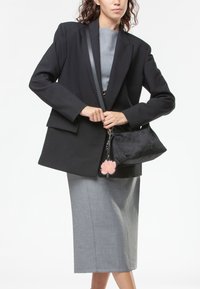 Zwarte oversized blazer over een grijze top, gecombineerd met een aansluitende grijze rok. Zwarte tas met een bloem sleutelbloem en textuuraccenten.