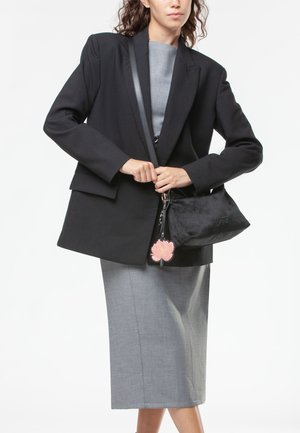 Blazer oversize nero sopra un top grigio, abbinato a una gonna grigia aderente. Borsa nera con portachiavi floreale e dettagli testurizzati.
