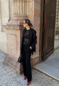 Čierny oversized blejzer na priesvitnom čiernom topu, skombinovaný so širokým čiernym nohavicami a bordovými lodičkami na päte. Obsahuje malú čiernu kabelku.