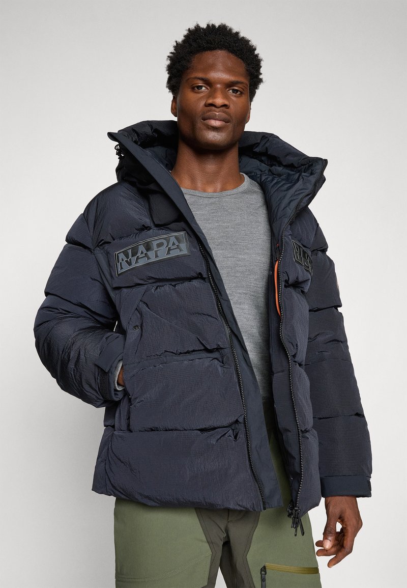 Veste rembourrée marine avec fermeture zippée à l'avant, capuche et logo en évidence. Tissu texturé avec des sections cousues et une finition mate. Comprend des poches pour les mains.