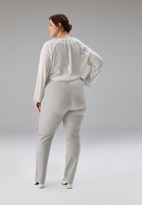 Weiße, leichte Bluse mit langen Ärmeln und gerafftem Ausschnitt, kombiniert mit hellgraßen, eng anliegenden Hosen. Glatter Stoff und maßgeschneidertes Design.