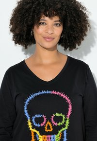 Schwarzes Langarmshirt mit V-Ausschnitt, das ein bunten Zickzack-Skelettdesign in neonfarbenen Tönen von Pink, Blau, Grün und Orange zeigt.