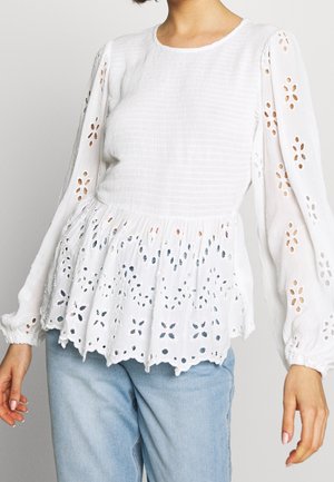 Biała bluzka z teksturowanego materiału z długimi, bufkami rękawami, zdobiona haftowanymi kwiatowymi wycięciami na dole i rękawach.