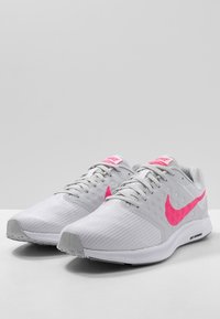 Scarpe da corsa Nike con tomaia in rete grigia, dettagli rosa e finitura testurizzata. Il design include un colletto imbottito e suola in gomma.