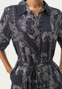 Rochie cămașă bleumarin, cu model paisley, mâneci scurte și curea. Material moale, cu buzunare, având accente florale intricate.