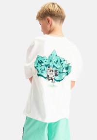 Witte katoenen t-shirt met een groot groen grafisch ontwerp op de achterkant, voorzien van gestileerde tekst en cartoonfiguren. Relaxed fit.