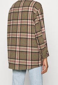 Chaqueta de camisa de cuadros verdes de gran tamaño, confeccionada en tejido texturizado, con líneas rosas y negras en un patrón de cuadros y detalles de puños con un solo botón.
