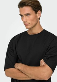 Camiseta negra de algodón con mangas cortas, cuello redondo y un corte relajado. La tela parece lisa con pocos detalles y bordes definidos.