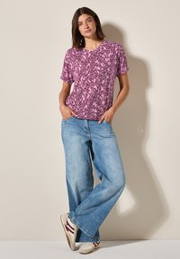 T-shirt à manches courtes en V imprimé floral rose, associé à un jean large bleu clair et des baskets beiges avec des accents bordeaux.