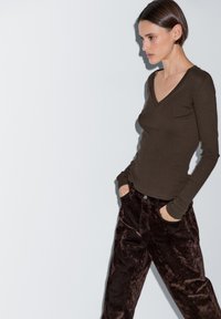 Brauner, gerippter Langarmoberteil mit V-Ausschnitt, kombiniert mit dunkelbraunen Samenhosen, die Seitentaschen und einen Knopfverschluss aufweisen.