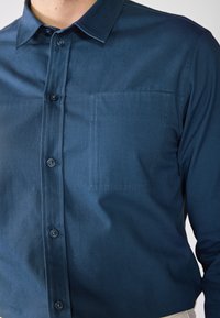 Camisa de botones azul marino, mezcla de algodón, que presenta un bolsillo en el pecho, collar puntiagudo, textura suave y botones en contraste.