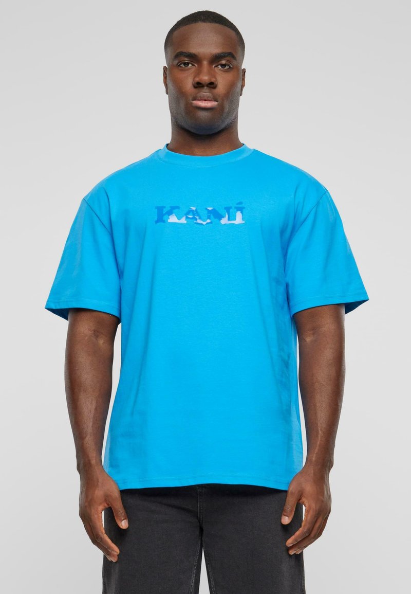 Bright blue cotton t-shirt with short sleeves and crew neck. Features a graphic print of the word "KANI" in varying blue tones across the chest.
