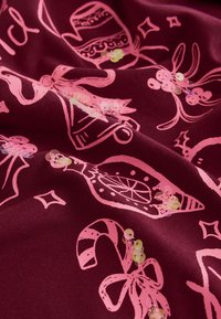 Roter Stoff mit pinkfarbenen, festlichen Motiven bedruckt, darunter Weihnachtskugeln und Zuckerstangen, mit verstreuten irisierenden Pailletten.