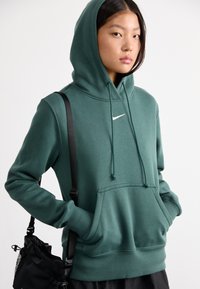 Donkergroen hoodie met een voork pocket, voorzien van een wit Nike-logo. Inclusief verstelbare trekkoorden en geribbelde manchetten.