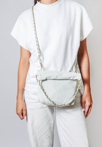 Borsa a tracolla in suede blu chiaro con design trapuntato, dotata di una tracolla a catena e una chiusura superiore piegata. Indossata in stile crossbody.