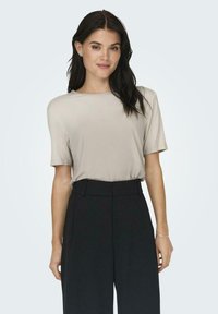 Light beige short-sleeve top, smooth fabric, relaxed fit, paired with high-waisted black trousers, featuring a tailored silhouette.